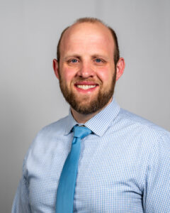 studio headshot of Alan Stout smiling and wearing a blue tie